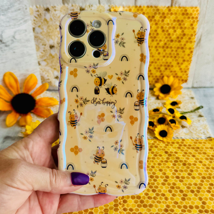Hand holding the Bee Happy Wavy Luxe MagSafe iPhone case with honeybees and rainbows on a honey-cream background