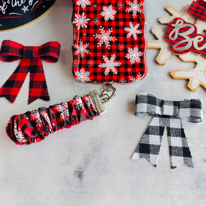 Buffalo Plaid Snowflake scrunchie phone wrist strap clipped to the matching iPhone case, with a Believe sign and buffalo check bows