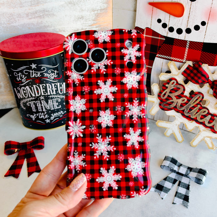 Hand holding the Buffalo Plaid Snowflake Wavy Luxe MagSafe iPhone case in red and black buffalo plaid with white snowflakes, with a Believe sign and buffalo check bows