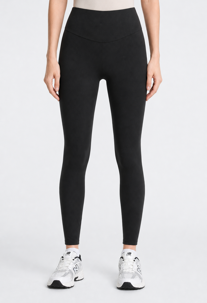 A model wearing black high-waisted leggings and white sneakers, shown from the waist down against a light gray studio background.
