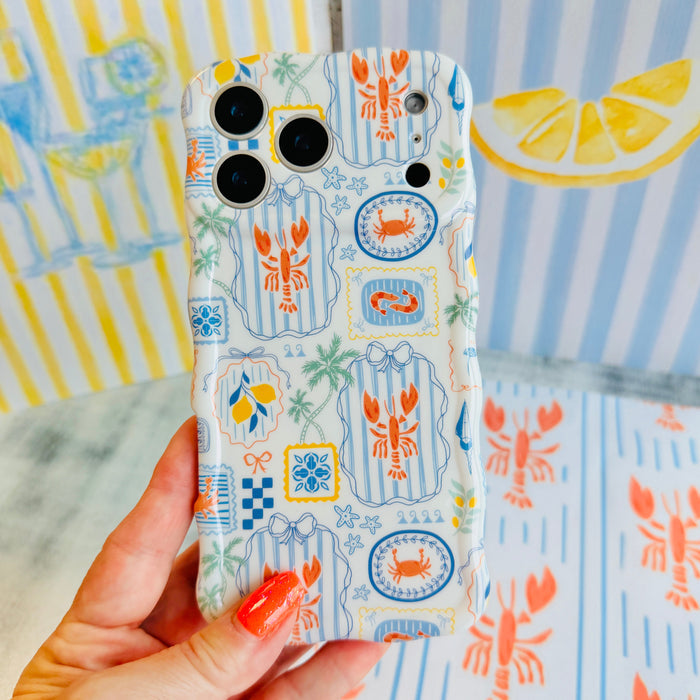 Hand holding the Coastal Catch Wavy Luxe MagSafe iPhone case with lobsters, crabs and blue tiles on a striped background