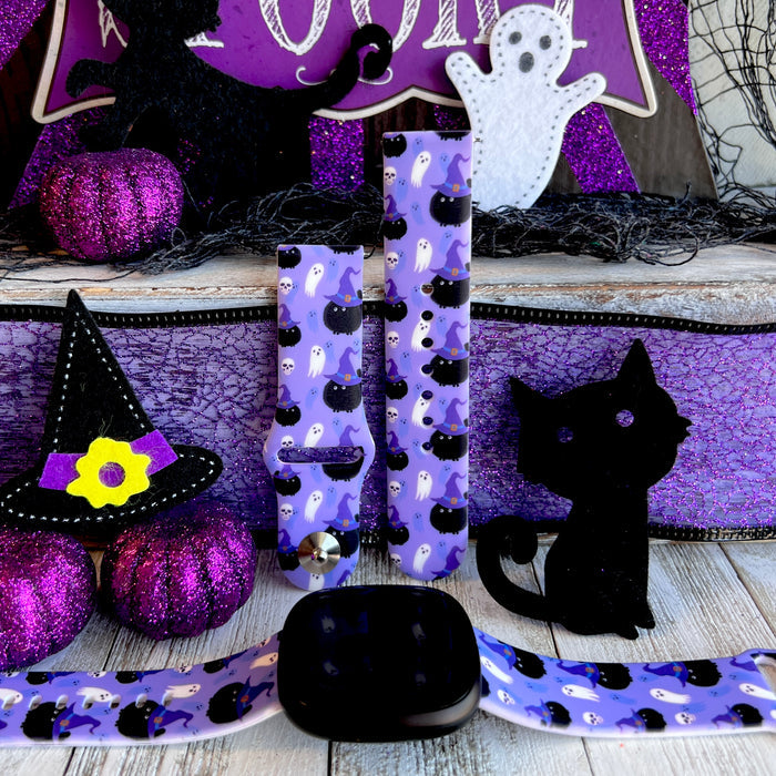 Ghostly Whisker's silicone Fitbit Versa 1/2 band hero shot in lavender with black witch-hat cats, ghosts and skulls, shown with a black Fitbit Versa.