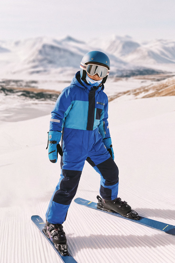 Child skiing on a groomed slope in the light and dark blue Deux par Deux PLAY one-piece snowsuit