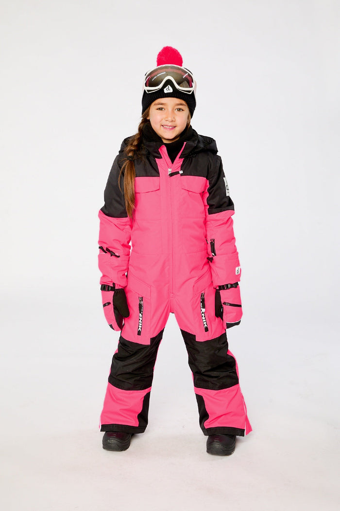 Child wearing the bright pink Deux par Deux TEKNIK one-piece snowsuit with ski goggles, front view