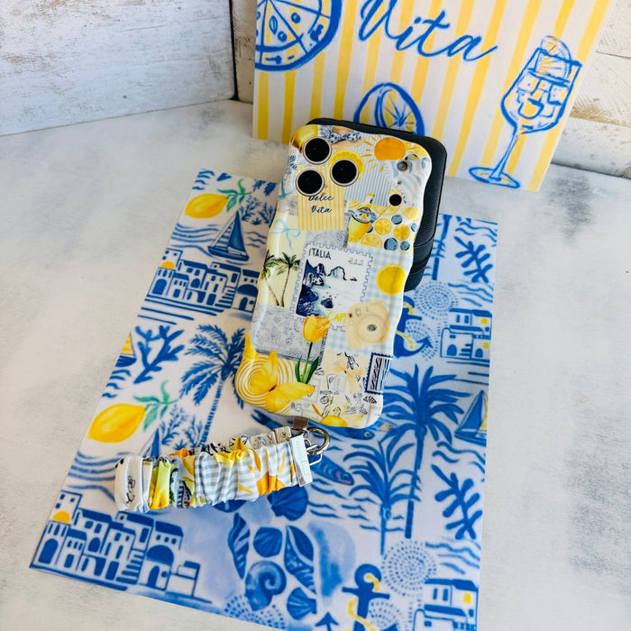 La Dolce Summer scrunchie phone wrist strap laid out with the matching Mediterranean lemon Wavy Luxe iPhone case