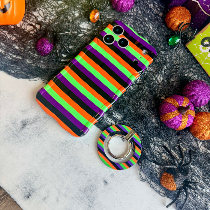 Main Witch Energy MagSafe grip ring lying beside the matching striped Wavy Luxe case, showing the black, purple, green and orange stripes on both.