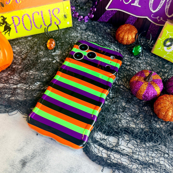 Main Witch Energy Wavy Luxe MagSafe iPhone case with bold black, purple, neon lime and orange witch-stocking stripes, styled with Halloween decor