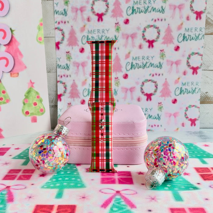 Merry Little Plaid Apple Watch band assembled and standing upright between glitter ornaments