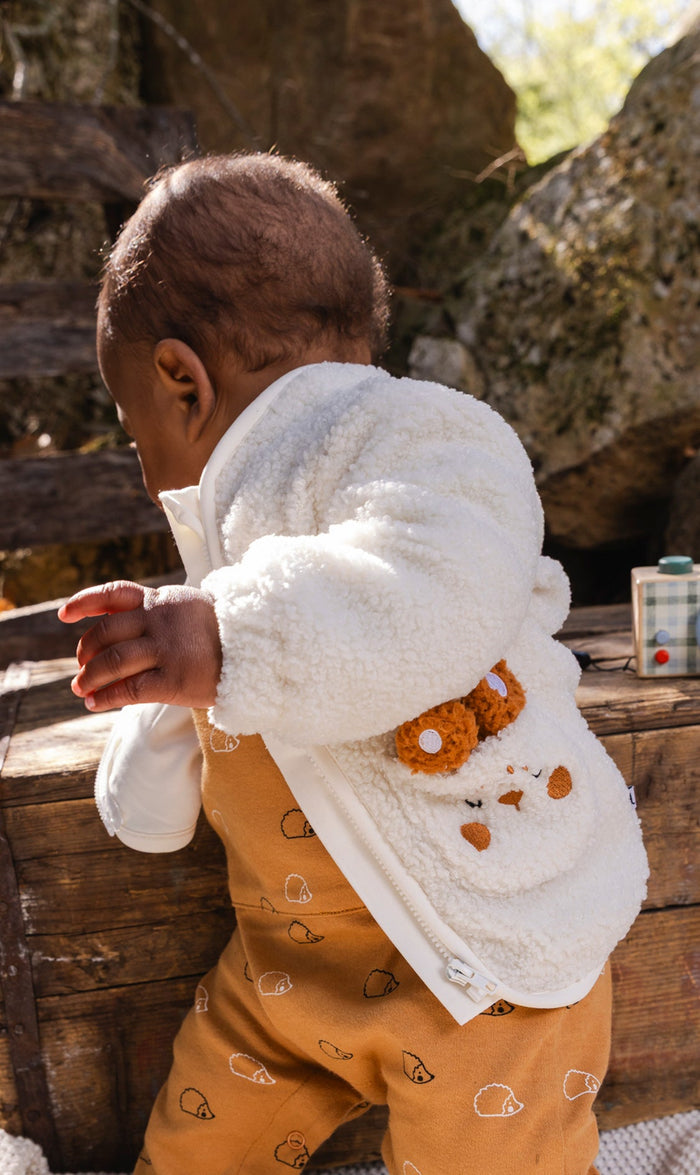 Baby wearing the off-white Deux par Deux sherpa jacket with bunny pocket outdoors