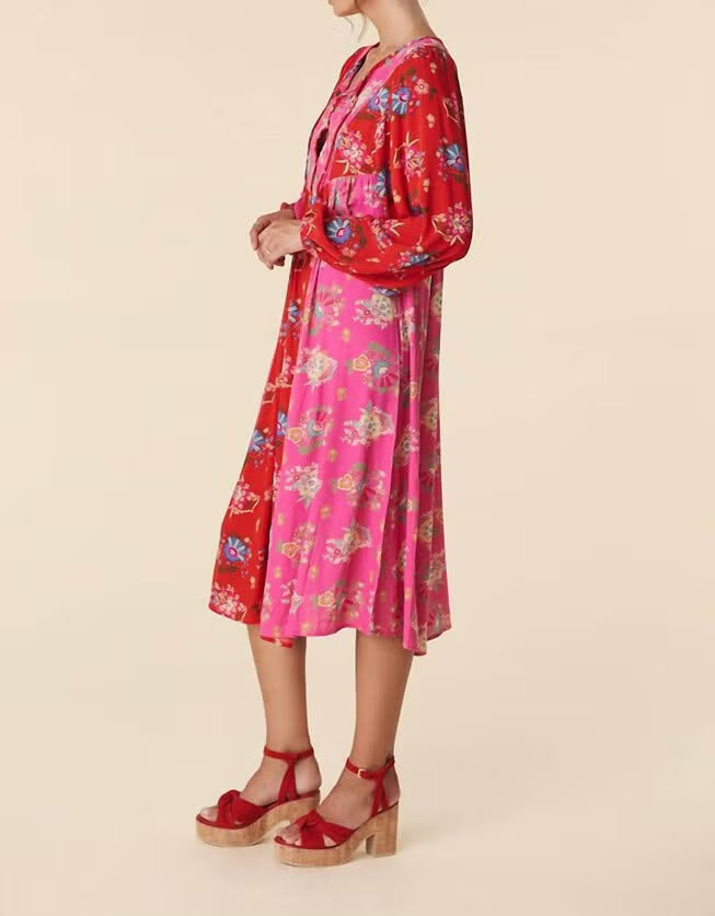 A woman modeling a long-sleeved midi dress with a vibrant red and pink floral print, paired with red platform sandals, against a solid beige background.