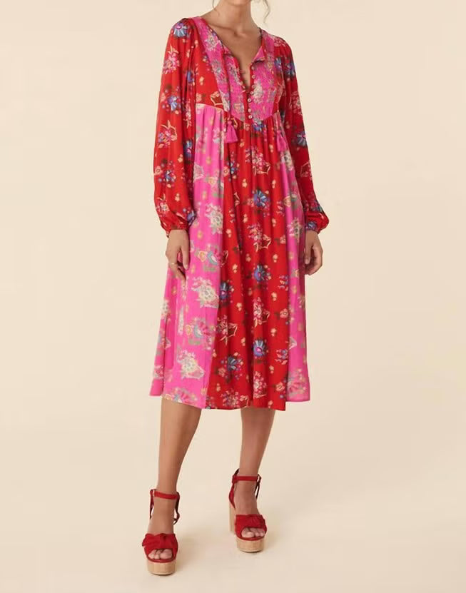 A woman modeling a long-sleeve midi dress with a vibrant red and pink floral print, paired with red platform sandals, against a solid beige background.
