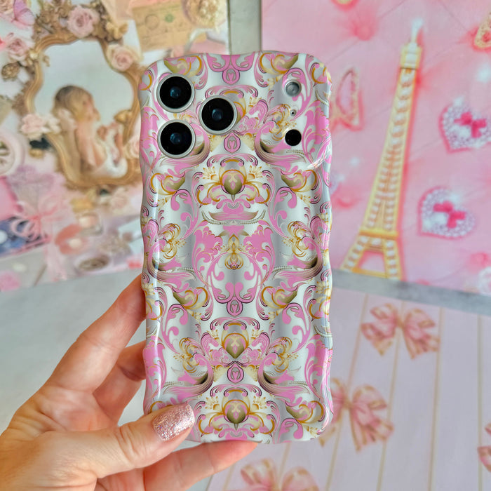 Hand holding The Pink Heiress pink and gold baroque Wavy Luxe iPhone case over a coquette flat lay with pink bows, a pearl Eiffel Tower and a gilded cherub mirror.
