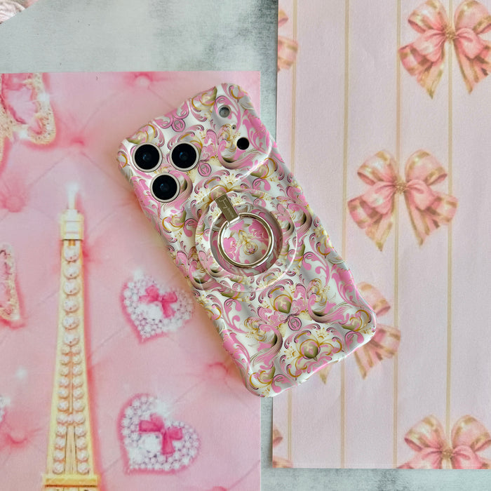 The Pink Heiress baroque iPhone case wearing the matching pink and gold MagSafe grip ring, styled on pink bows with a pearl Eiffel Tower and a heart trinket.
