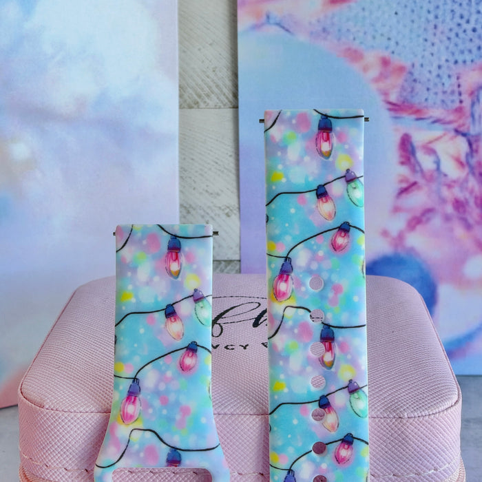 Close-up of both Twinkle All The Way Samsung Galaxy Watch band straps with pastel Christmas string lights on aqua