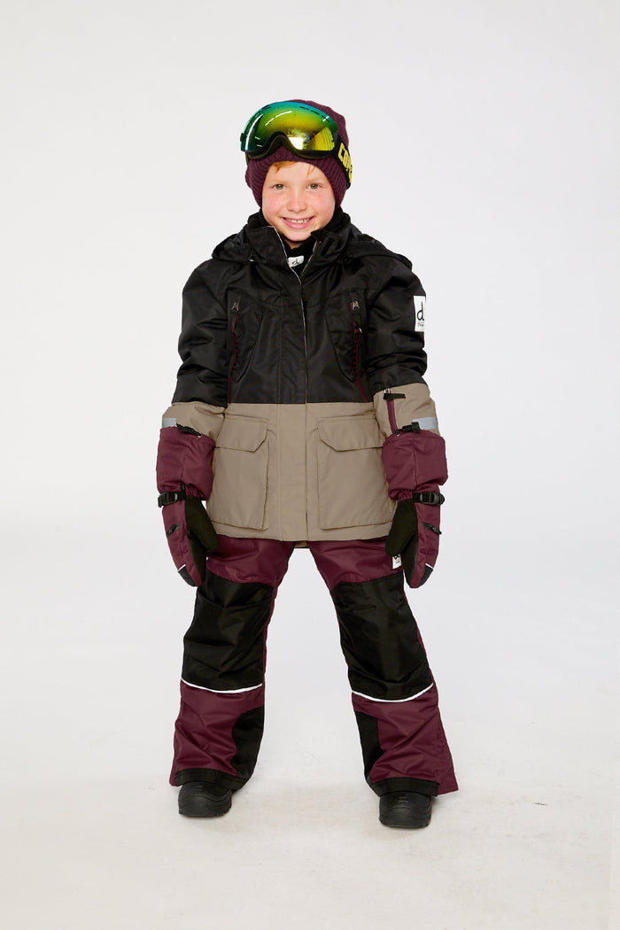 Child wearing the black, beige and burgundy Deux par Deux TEKNIK two-piece snowsuit, front view