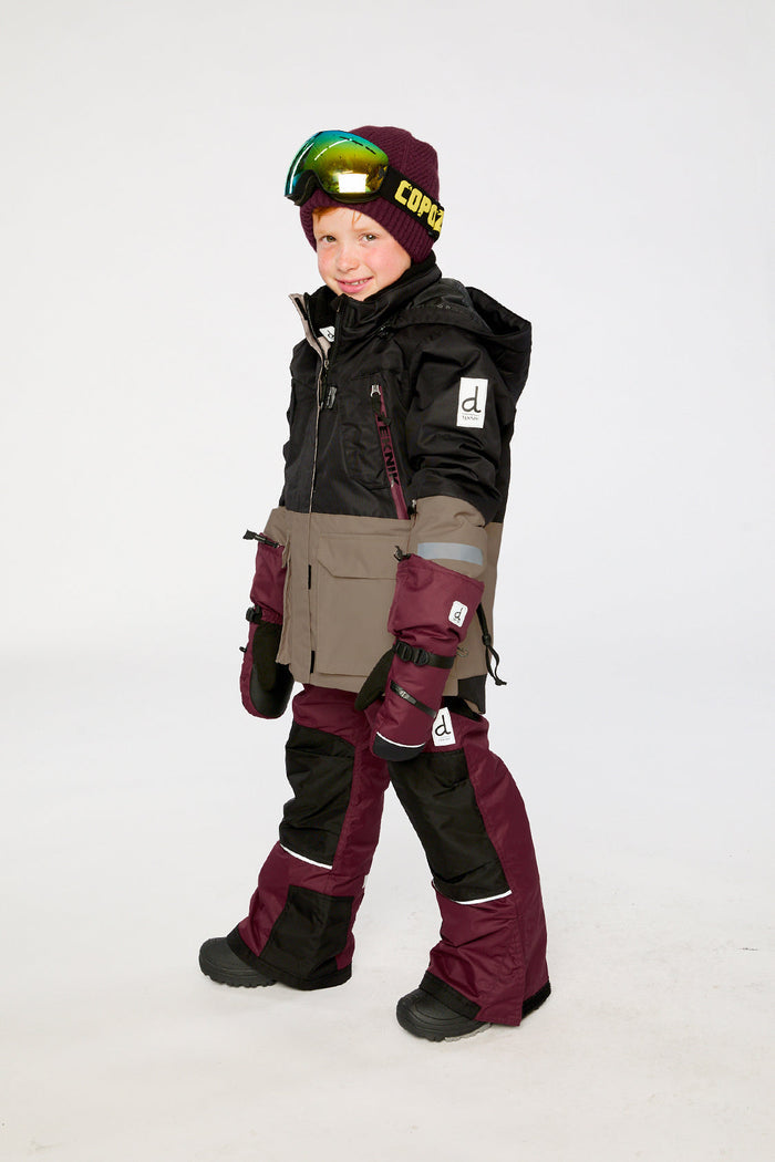 Child wearing the black, beige and burgundy Deux par Deux TEKNIK two-piece snowsuit, side view