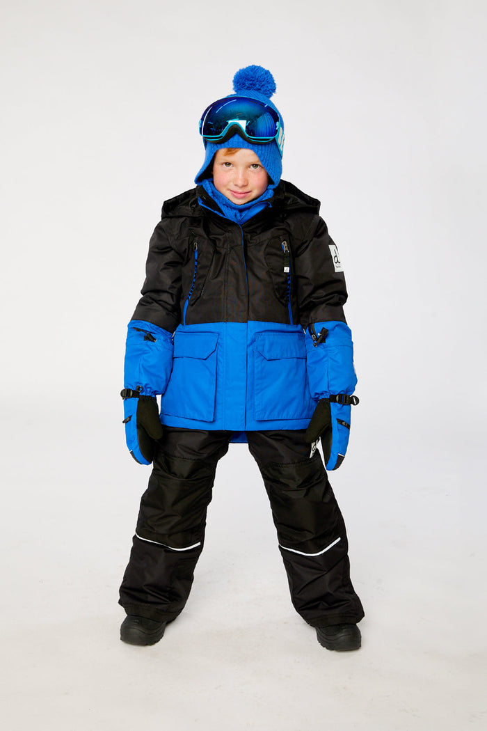 Child wearing the black and royal blue Deux par Deux TEKNIK two-piece snowsuit with goggles, front view