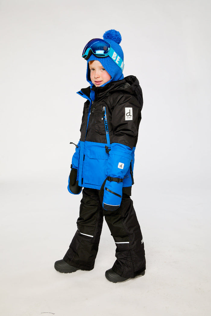 Child wearing the black and royal blue Deux par Deux TEKNIK two-piece snowsuit, side view